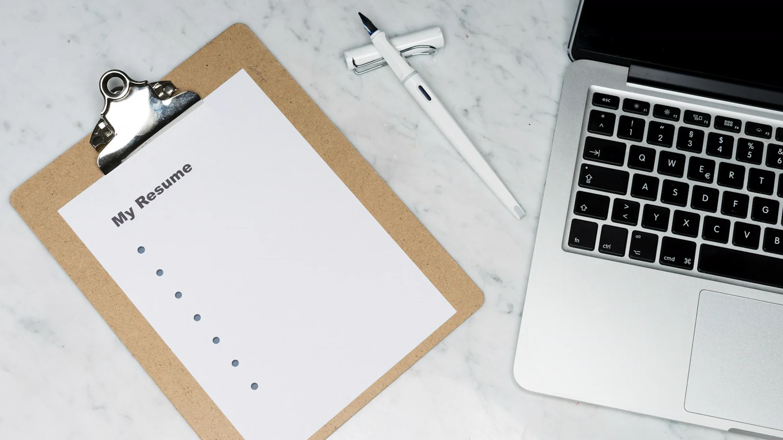 Un portapapeles con una plantilla de CV en blanco junto a un portátil — el punto de partida clásico 